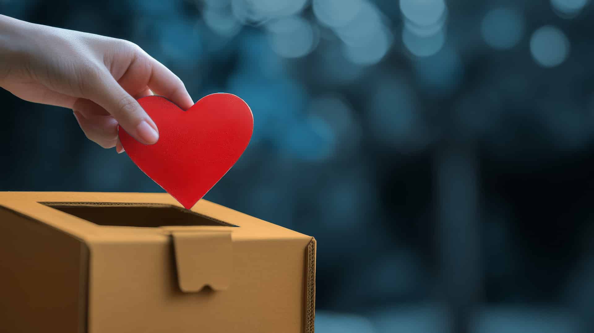 A hand placing a red paper heart into a donation box