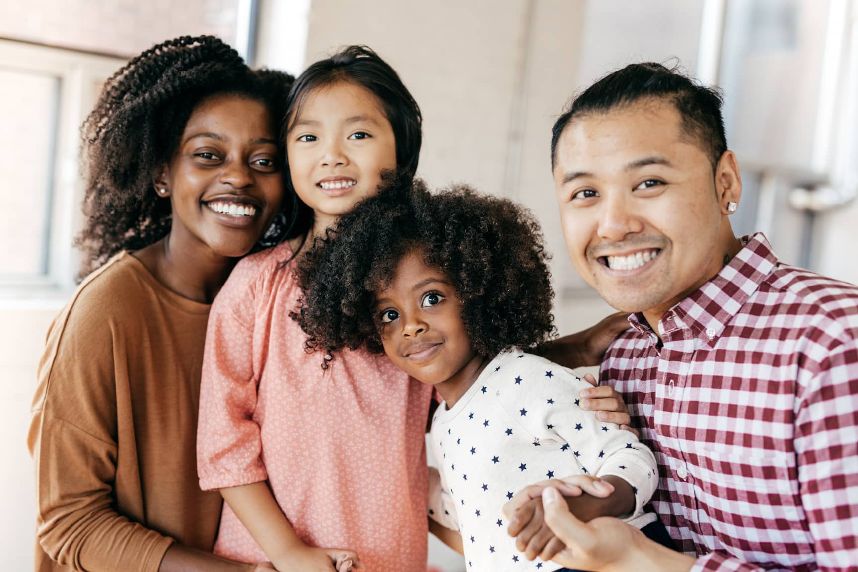 An interracial family smiling for a picture of an Asian father, a black mother, and their two daughters.